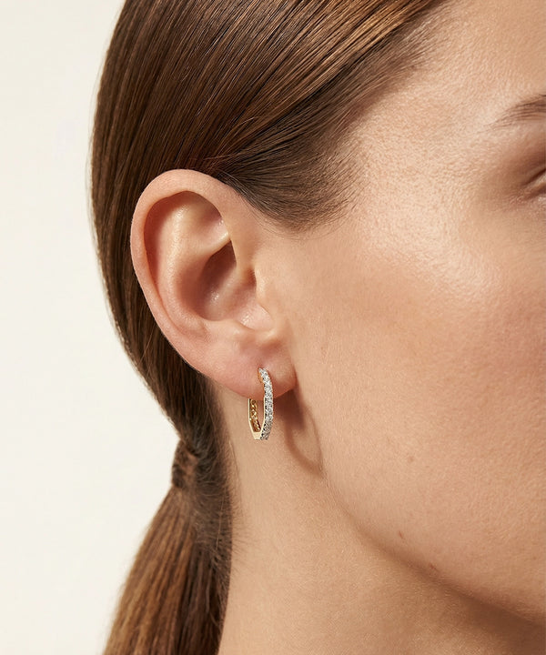 Close-up of a person wearing a diamond hoop earring on a neutral background