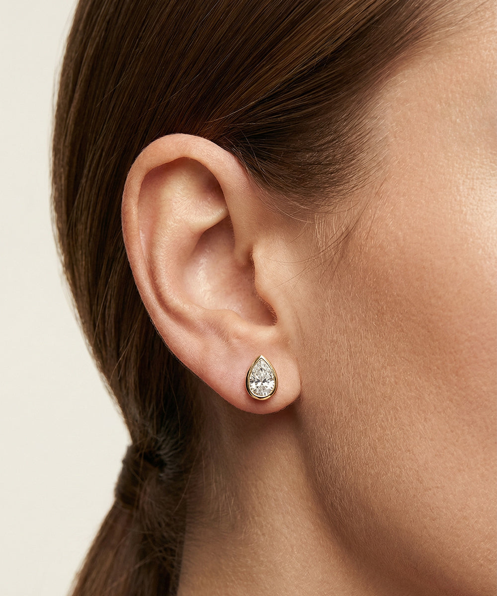 Teardrop-shaped earring worn by a person with a neutral background