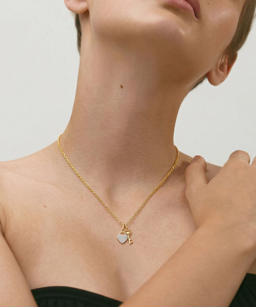 Gold necklace with heart and key pendant worn by a person on a neutral background