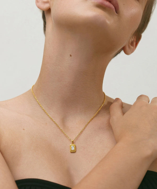 Gold necklace with a pendant on a person against a neutral background