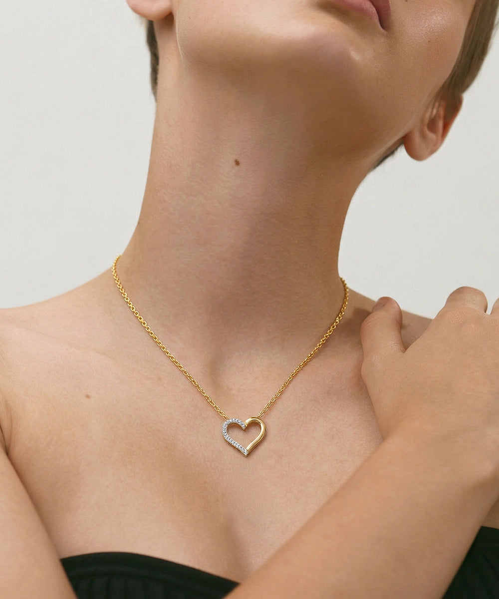 Gold necklace with a heart-shaped pendant worn by a person against a neutral background