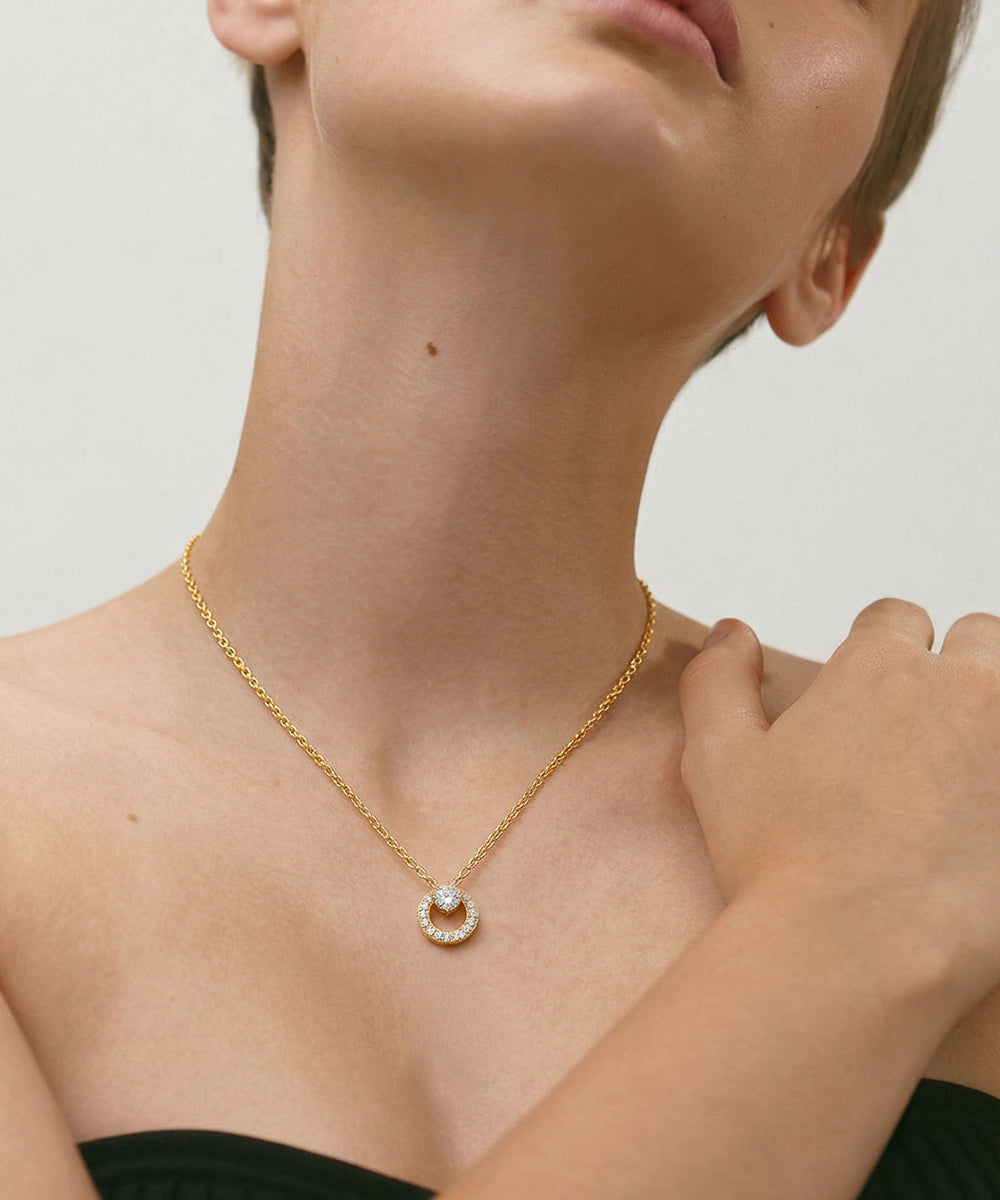 Gold necklace with a circular pendant worn by a person against a neutral background