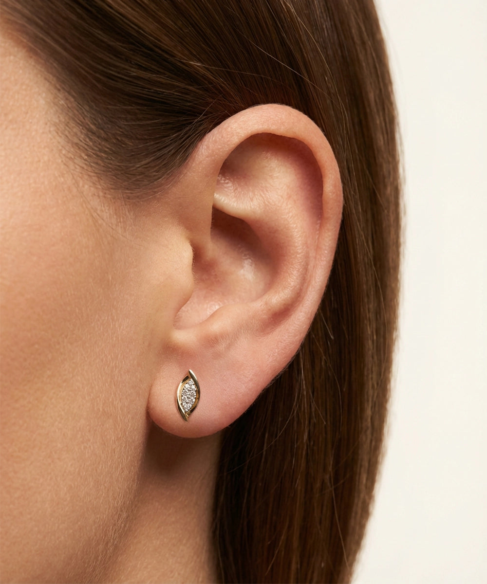Close-up of an ear wearing a diamond earring on a neutral background