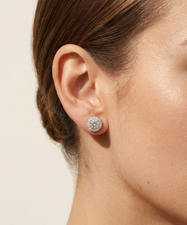 Close-up of an ear wearing a diamond stud earring on a neutral background