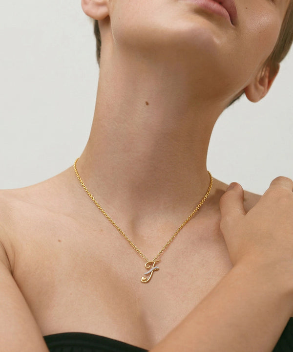 Gold necklace with a letter 'J' pendant on a person against a neutral background