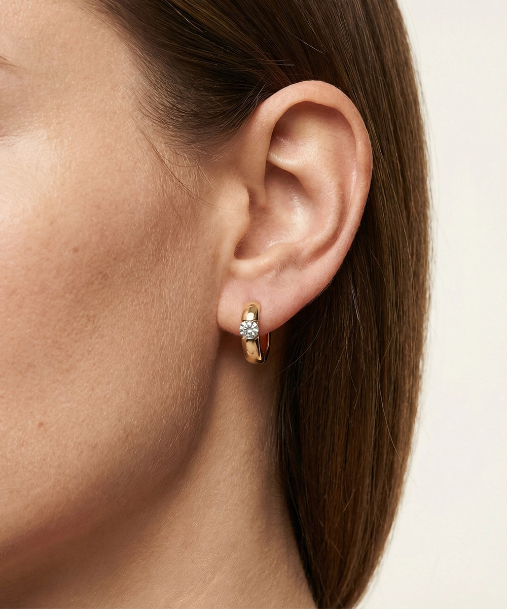 Close-up of an ear wearing a small hoop earring with a neutral background