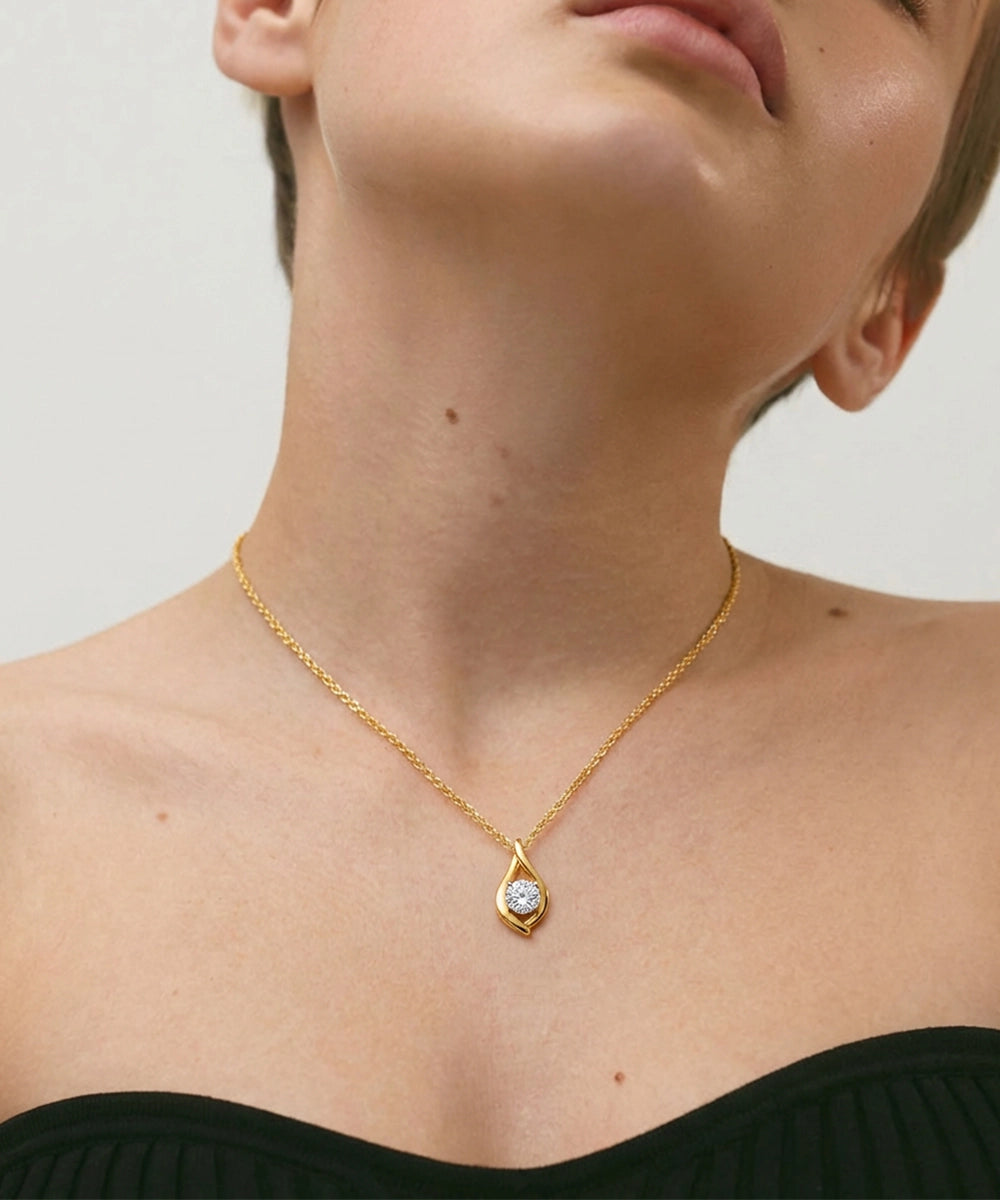 Gold necklace with a diamond pendant worn by a person against a neutral background