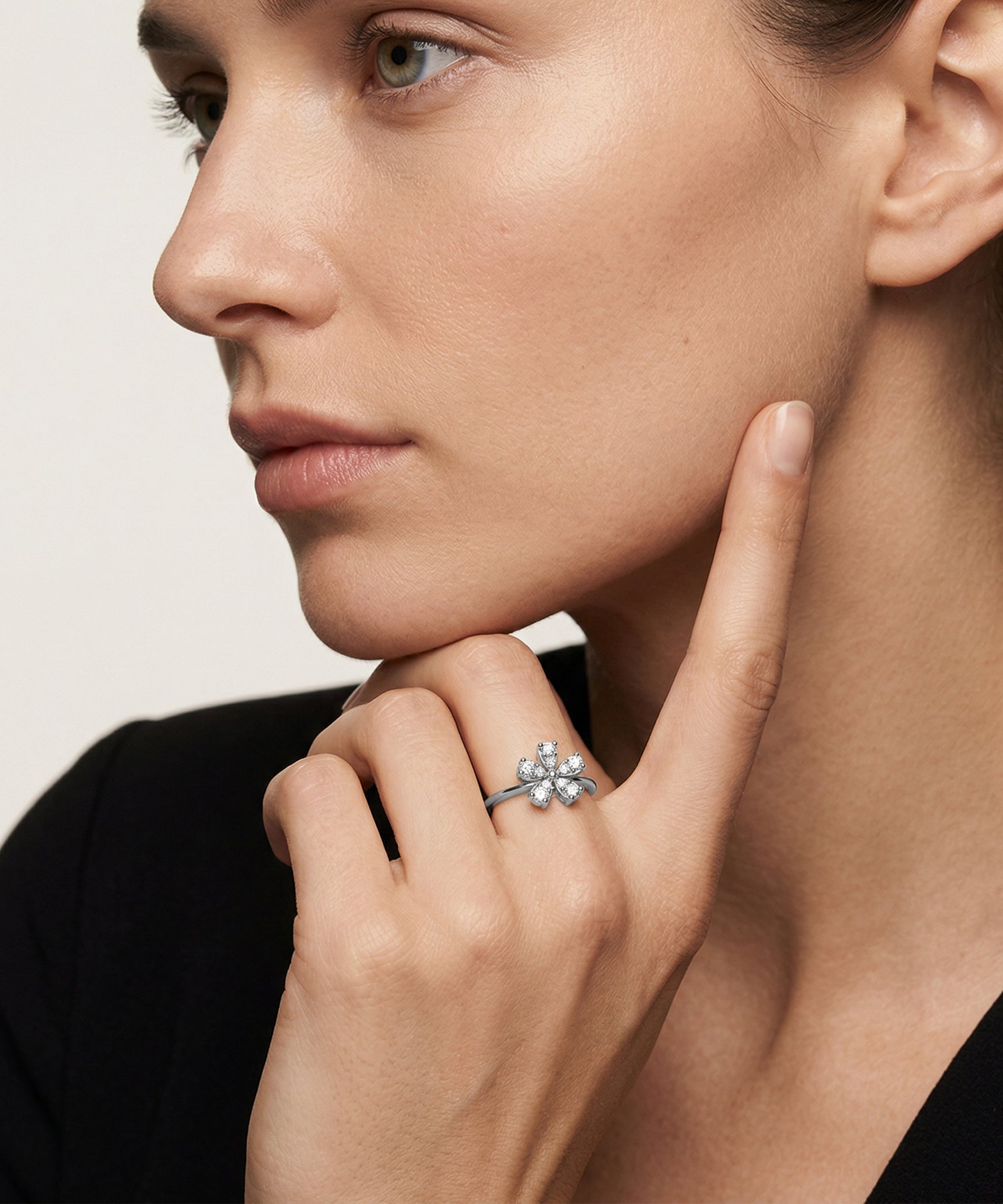 Close-up of a woman wearing a diamond ring on her finger against a neutral background