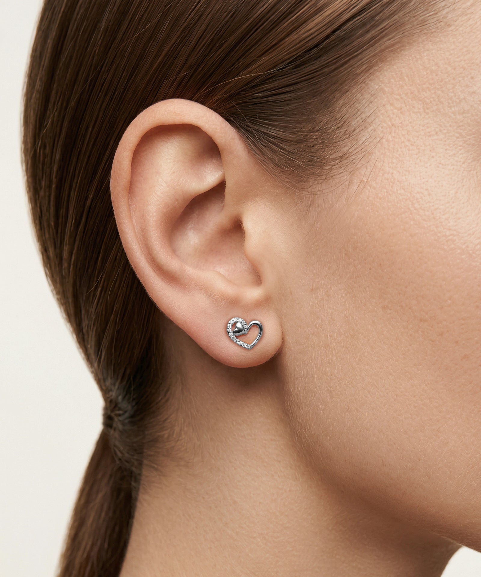 Close-up of an ear wearing a heart-shaped earring with a white background