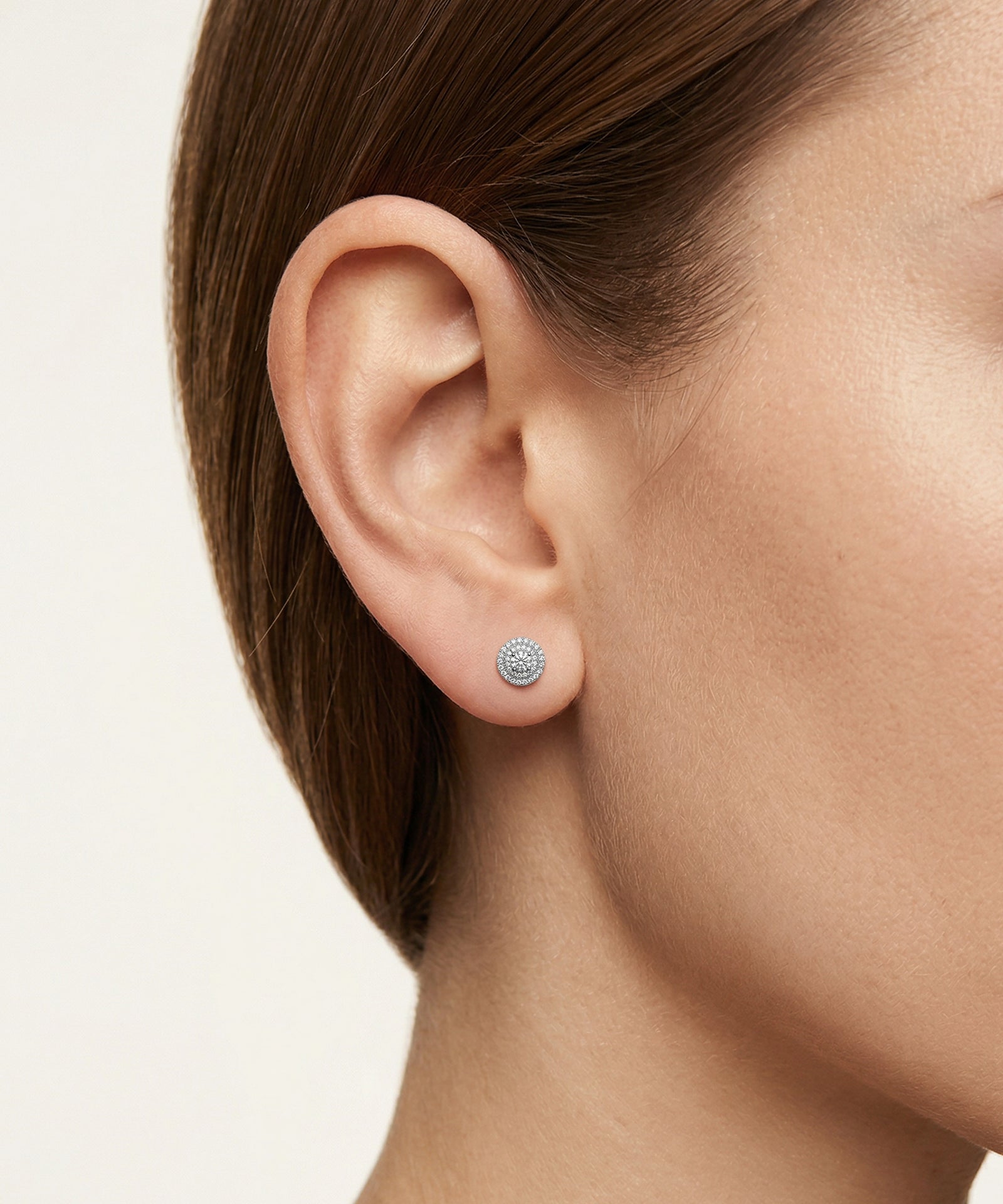 Close-up of an ear wearing a silver earring with a clear gemstone on a neutral background