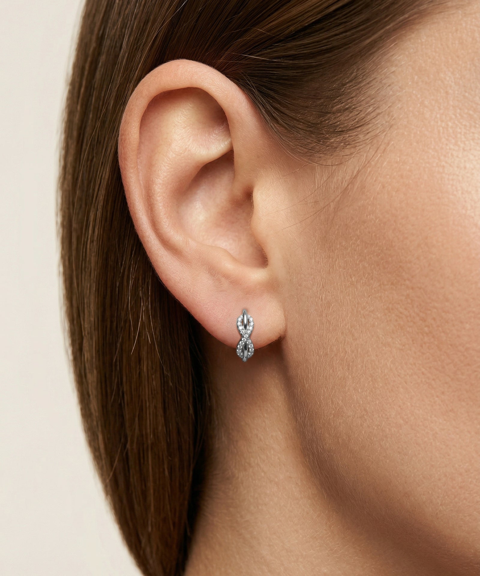 Close-up of an ear wearing a diamond earring on a neutral background