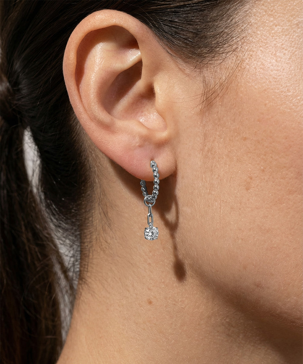Close-up of an ear wearing a silver hoop earring with a small round pendant.