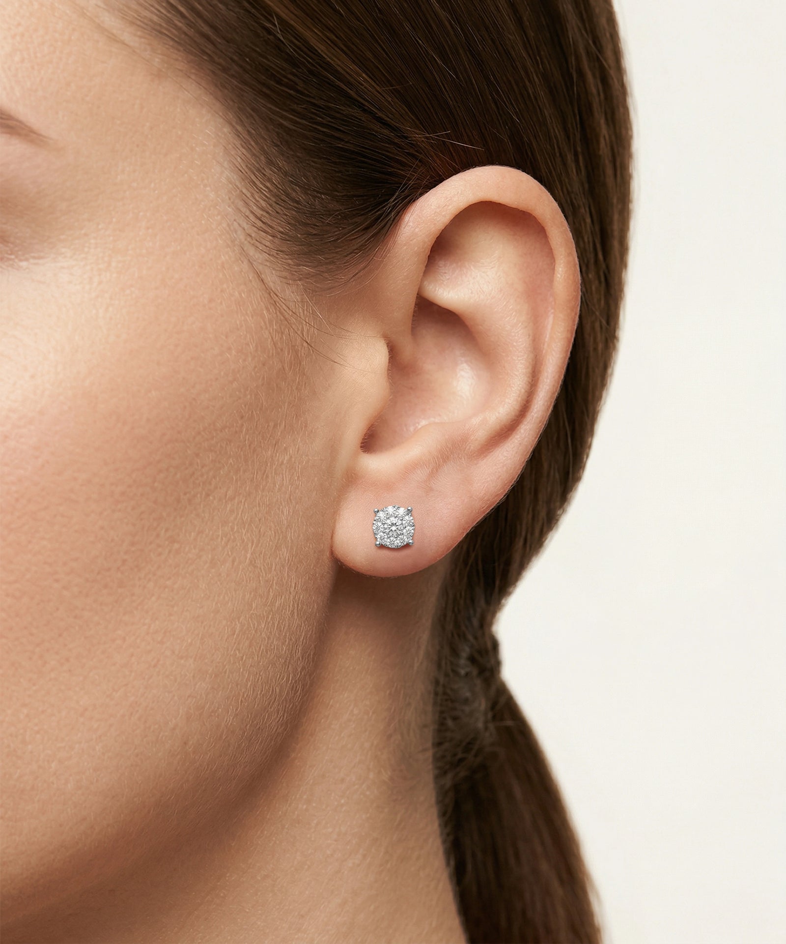 Close-up of an ear wearing a diamond earring with a neutral background