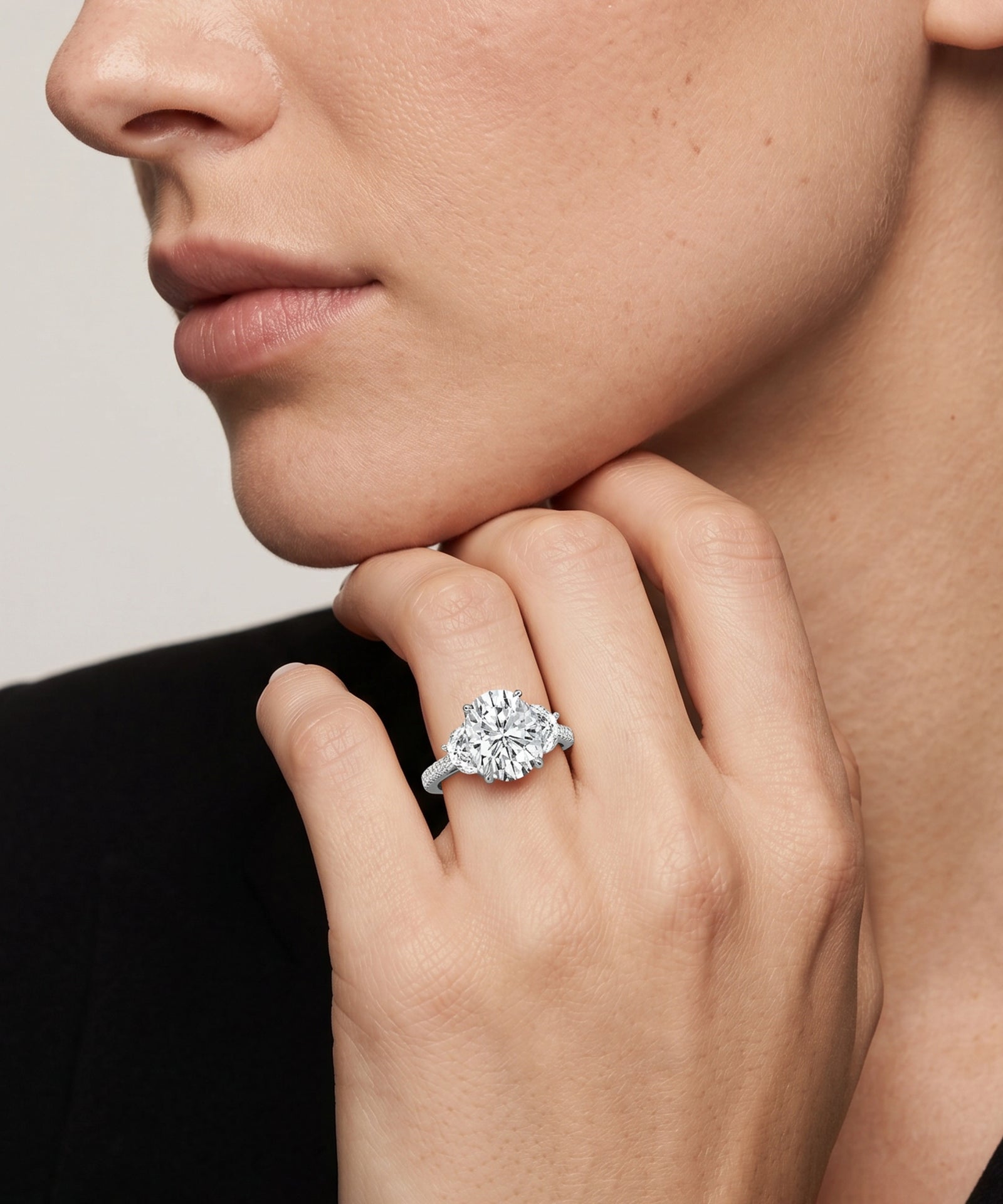 Close-up of a hand wearing a diamond ring with a neutral background