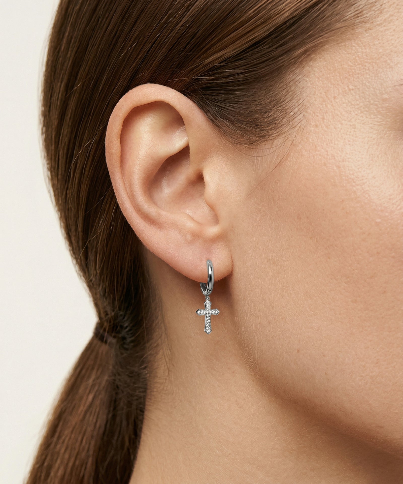 Close-up of an ear wearing a silver cross earring with a blurred background
