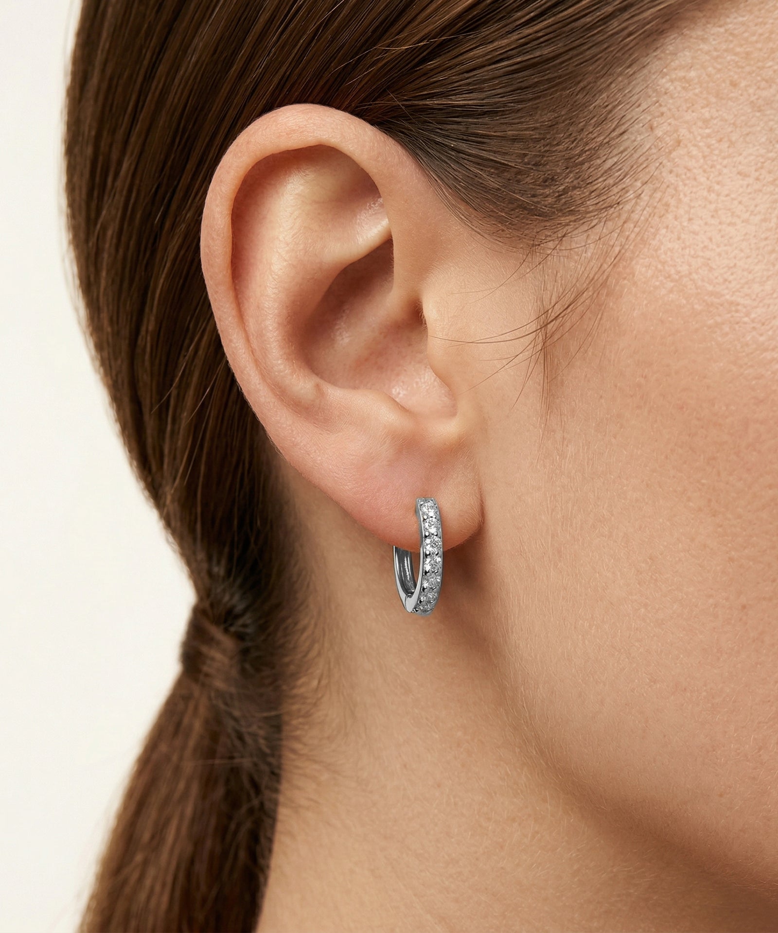 Close-up of an ear wearing a silver hoop earring with a blurred background