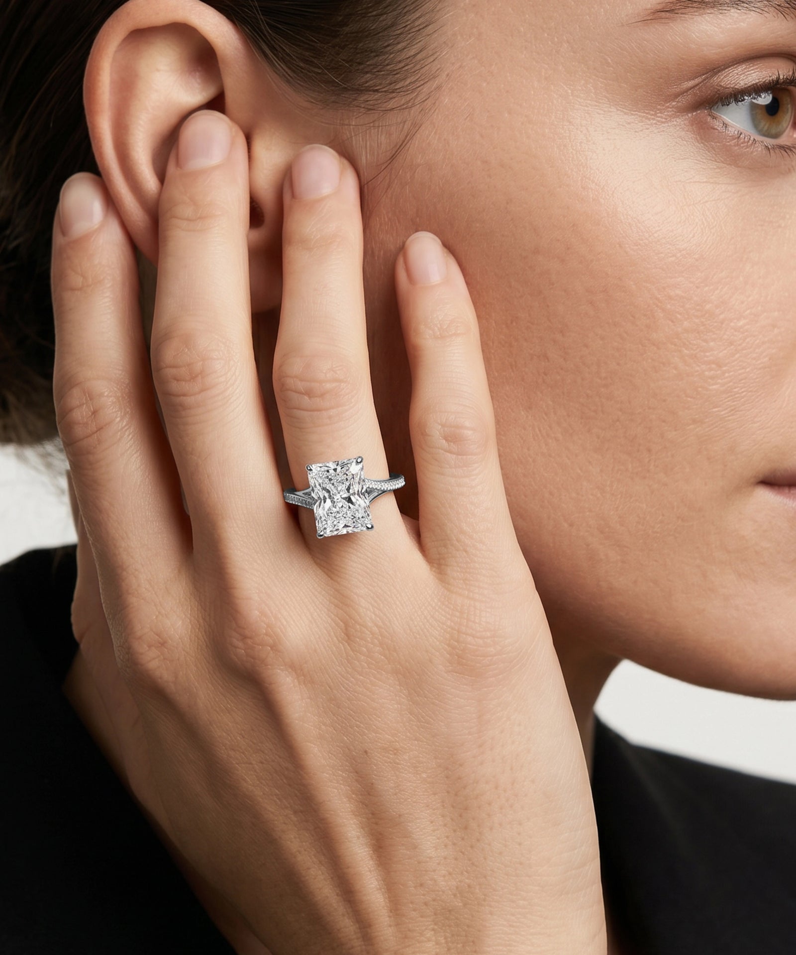 Close-up of a hand with a diamond ring near an ear, with a blurred background