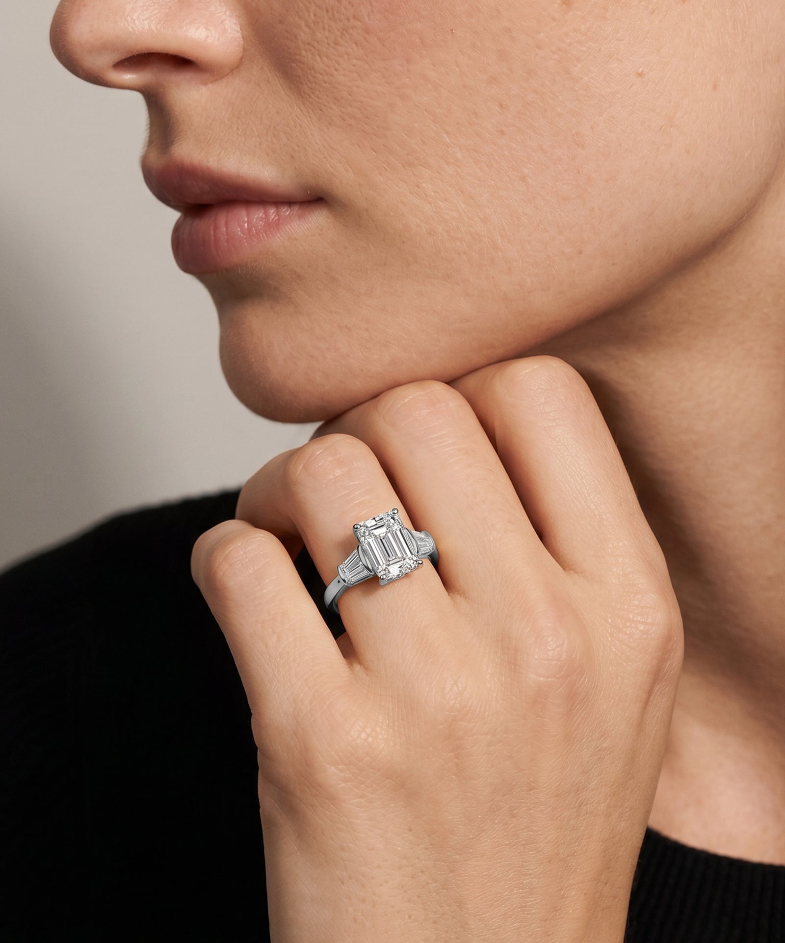Close-up of a hand wearing a diamond ring with a neutral background