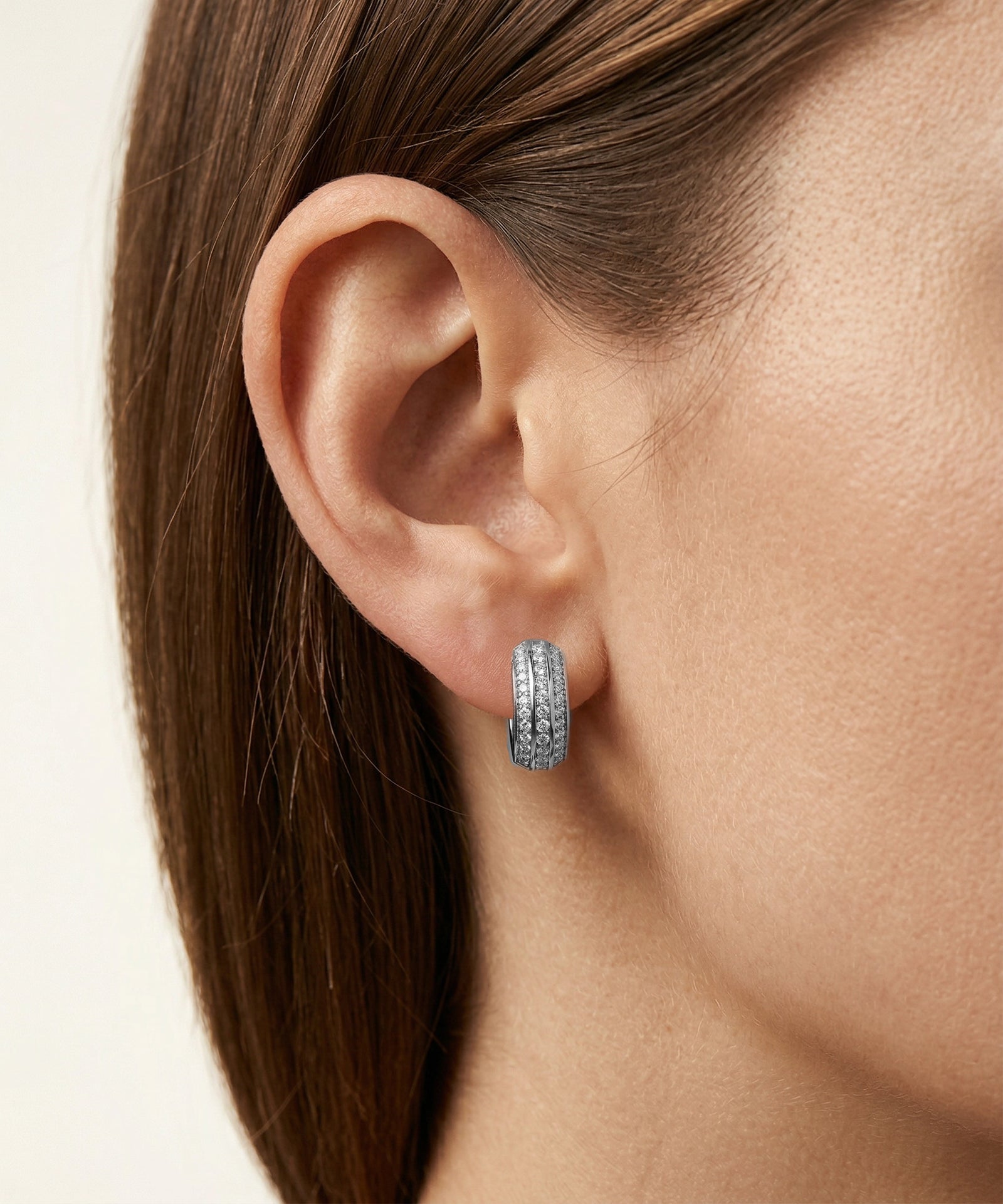 Close-up of an ear wearing a silver hoop earring with a neutral background