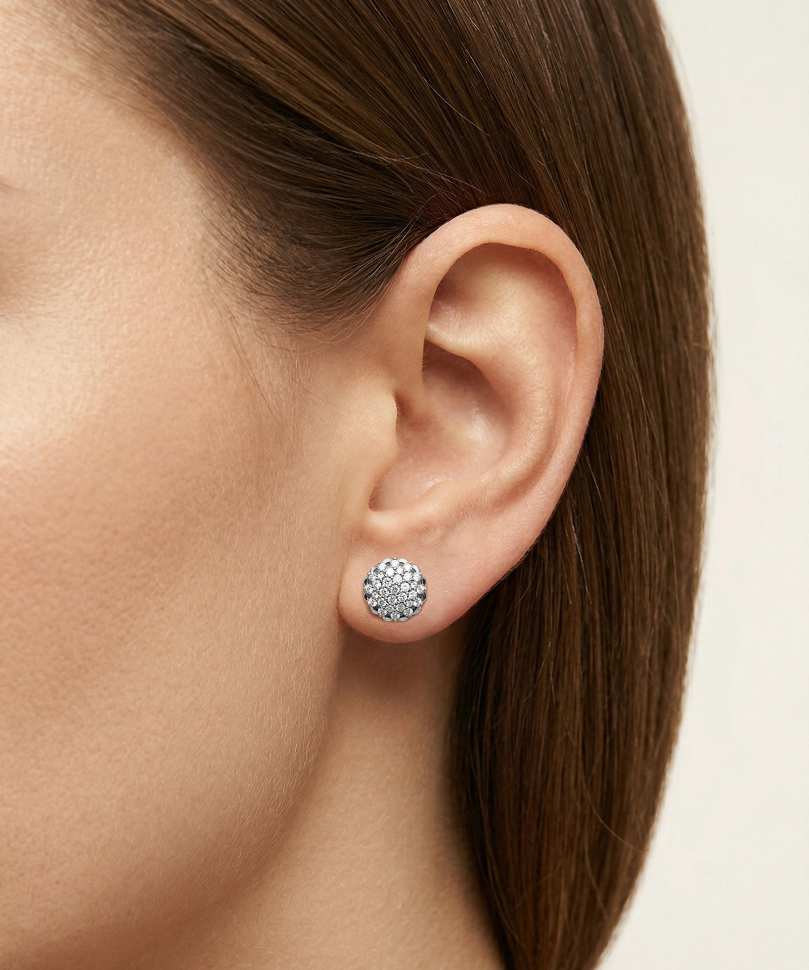 Close-up of an ear wearing a round silver earring with clear stones on a neutral background