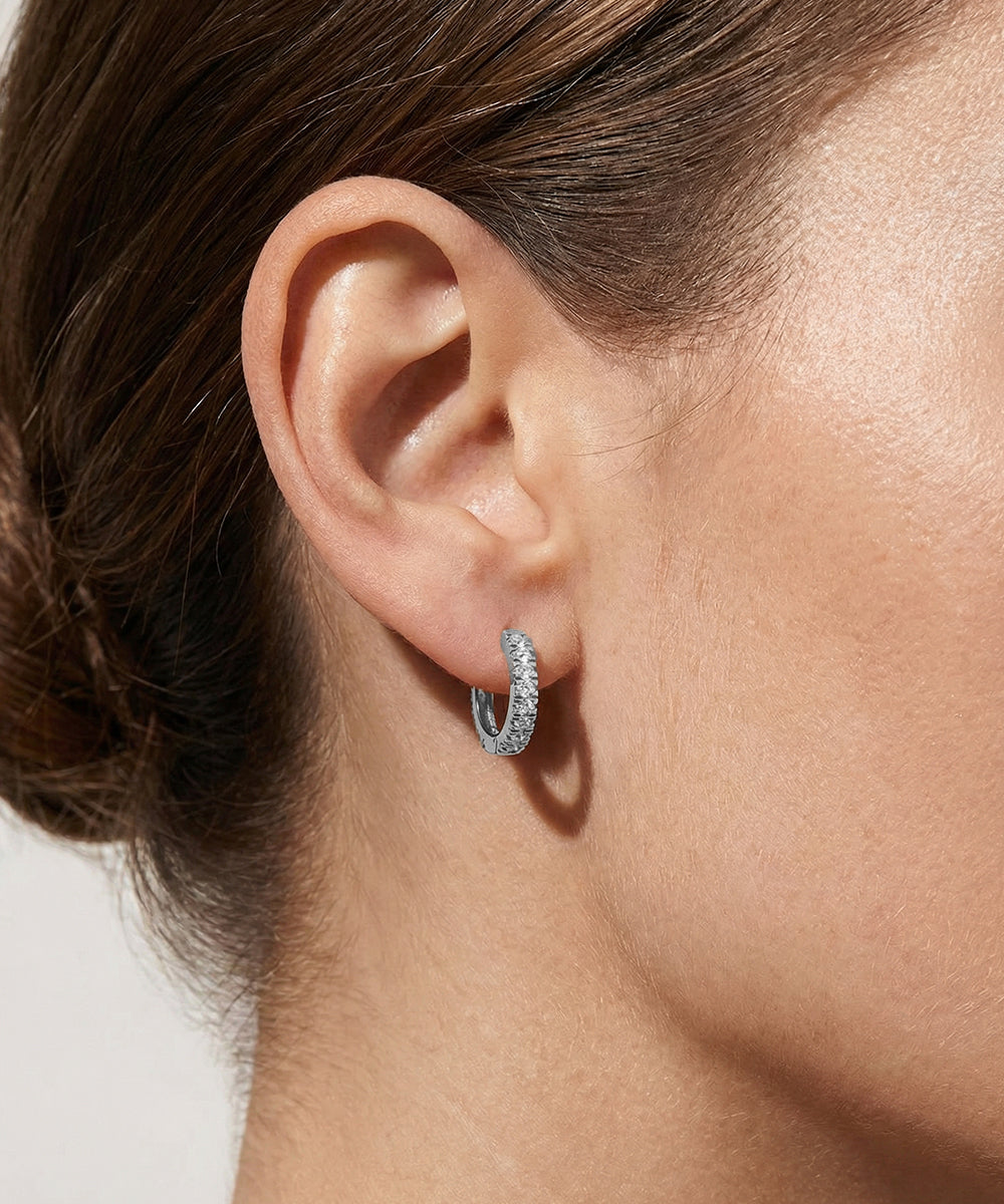 Close-up of an ear wearing a silver hoop earring with a neutral background