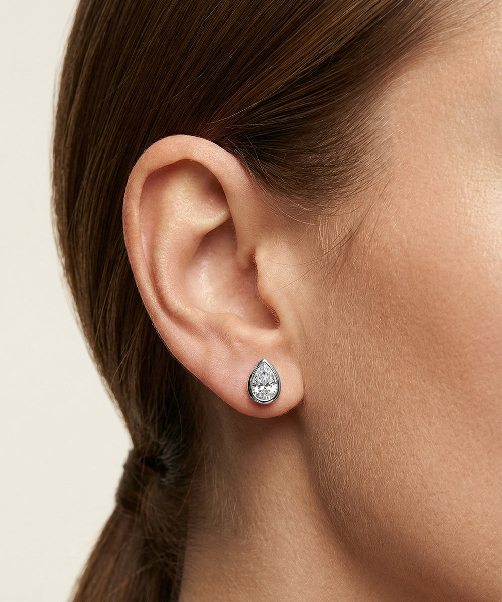 Teardrop-shaped diamond earring worn by a person with a neutral background