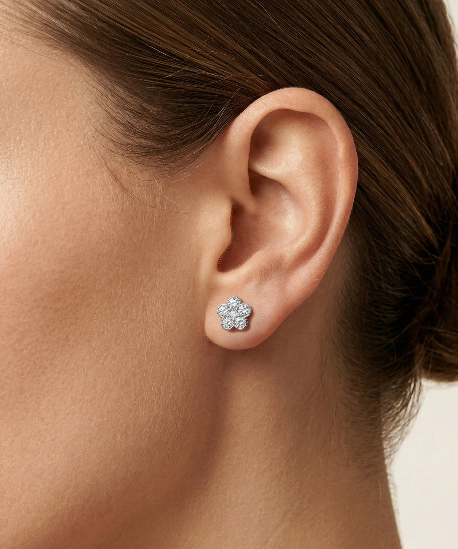 Close-up of an ear wearing a diamond stud earring with a blurred background