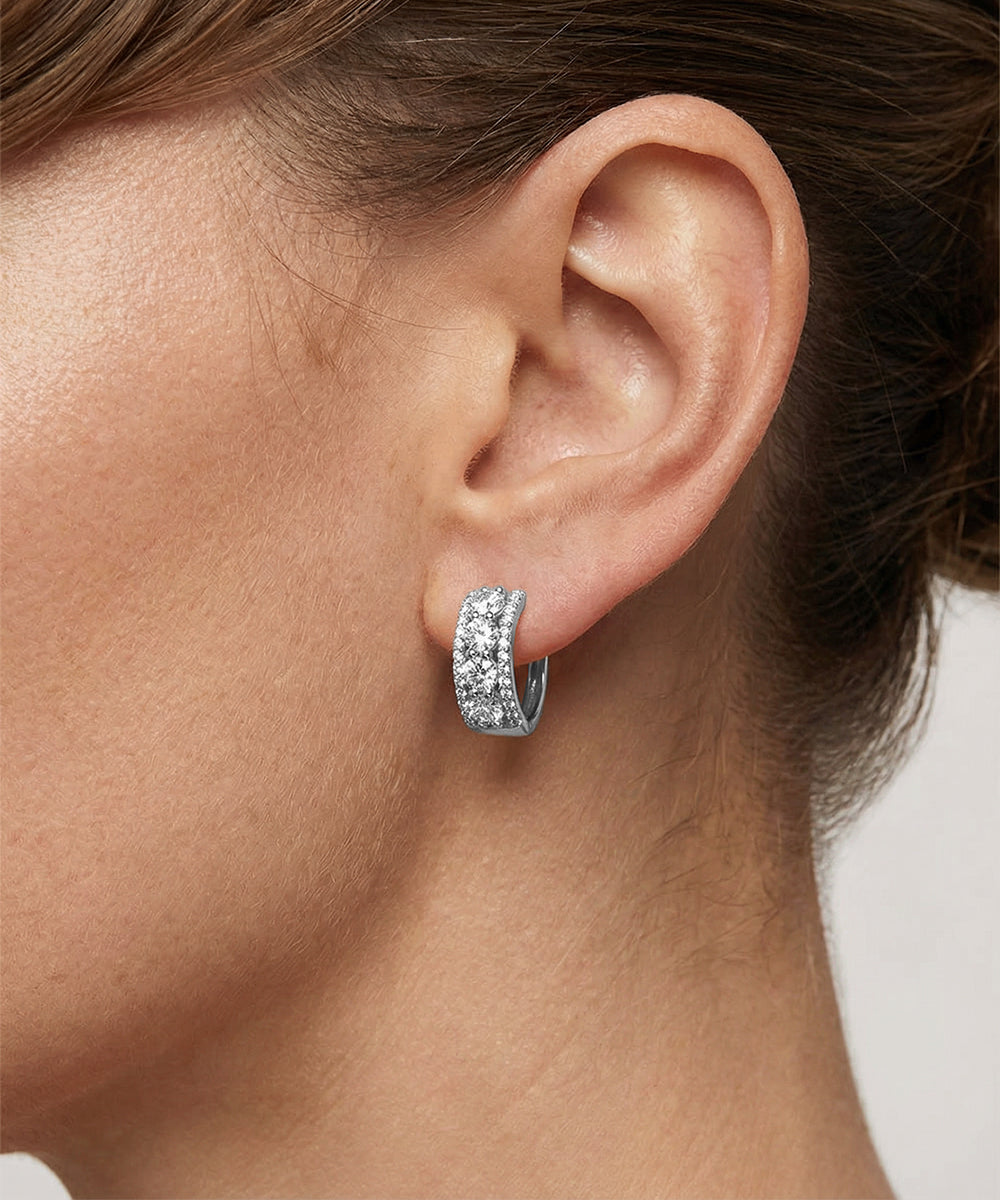 Close-up of an ear wearing a silver hoop earring with clear gemstones.