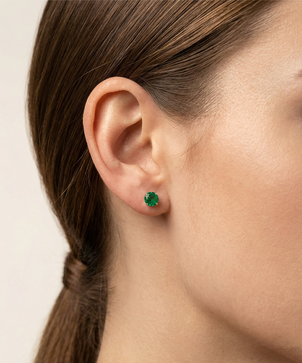 Close-up of a person wearing green gemstone earrings with a neutral background