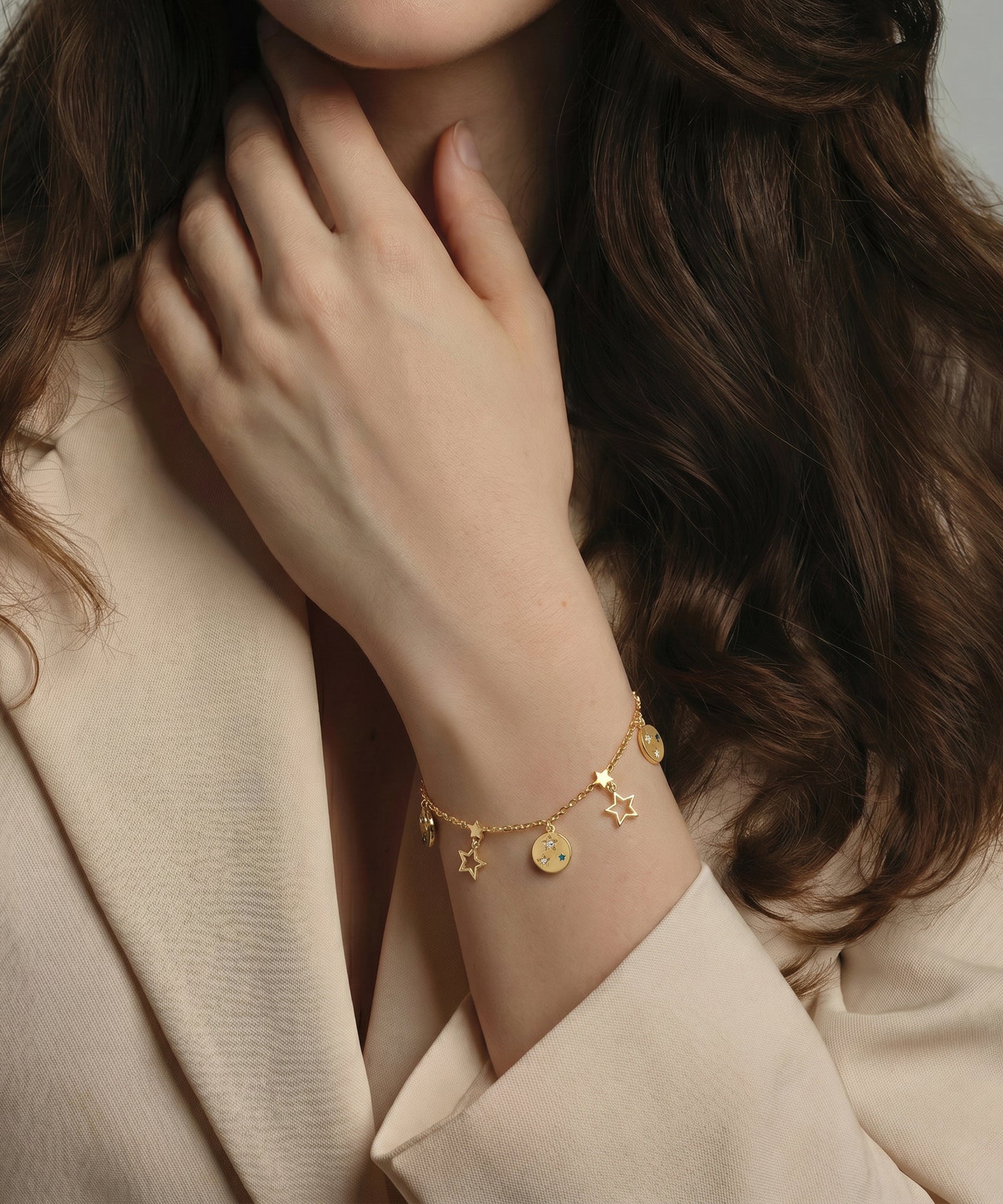 Gold bracelet with star and coin charms on a person wearing a beige coat.