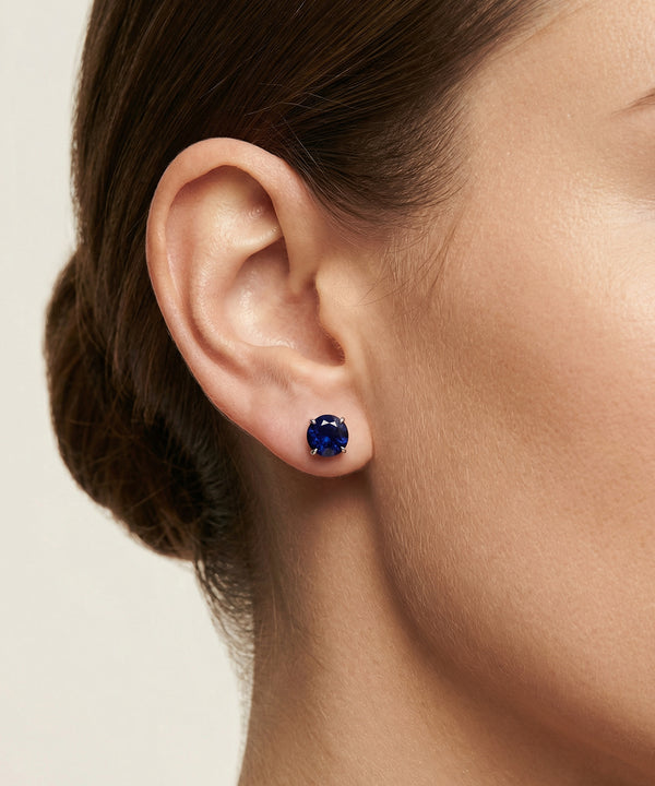 Close-up of an ear wearing a blue gemstone earring on a neutral background