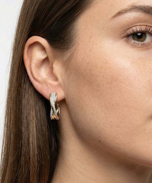 Close-up of a woman wearing a gold hoop earring with a white stone.