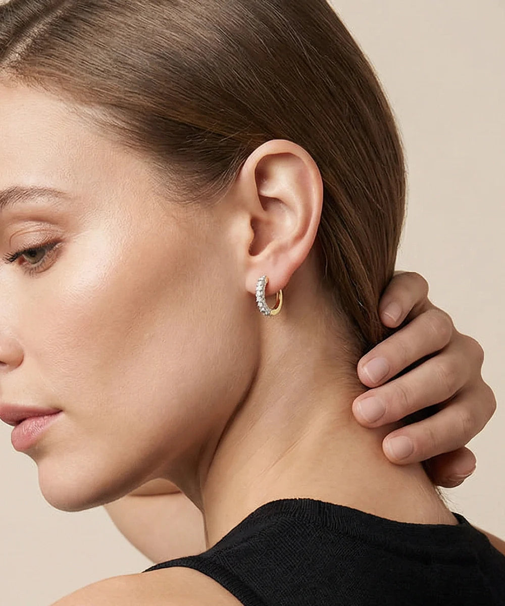 Close-up of a woman wearing gold hoop earrings with a neutral background