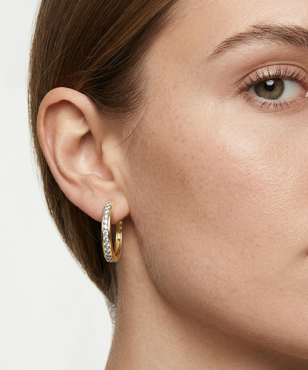 Close-up of a woman's ear wearing a silver hoop earring with a blurred background