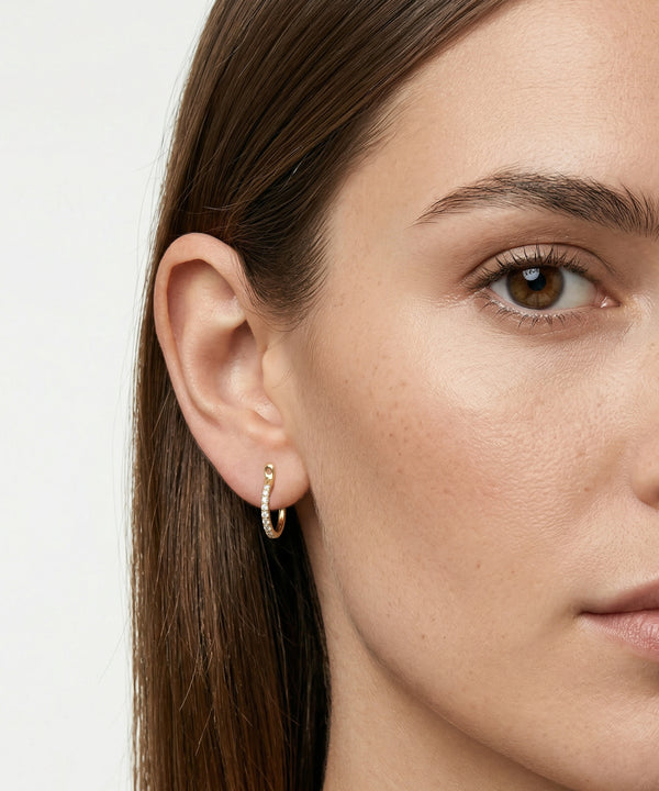 Close-up of a woman wearing a gold hoop earring against a neutral background