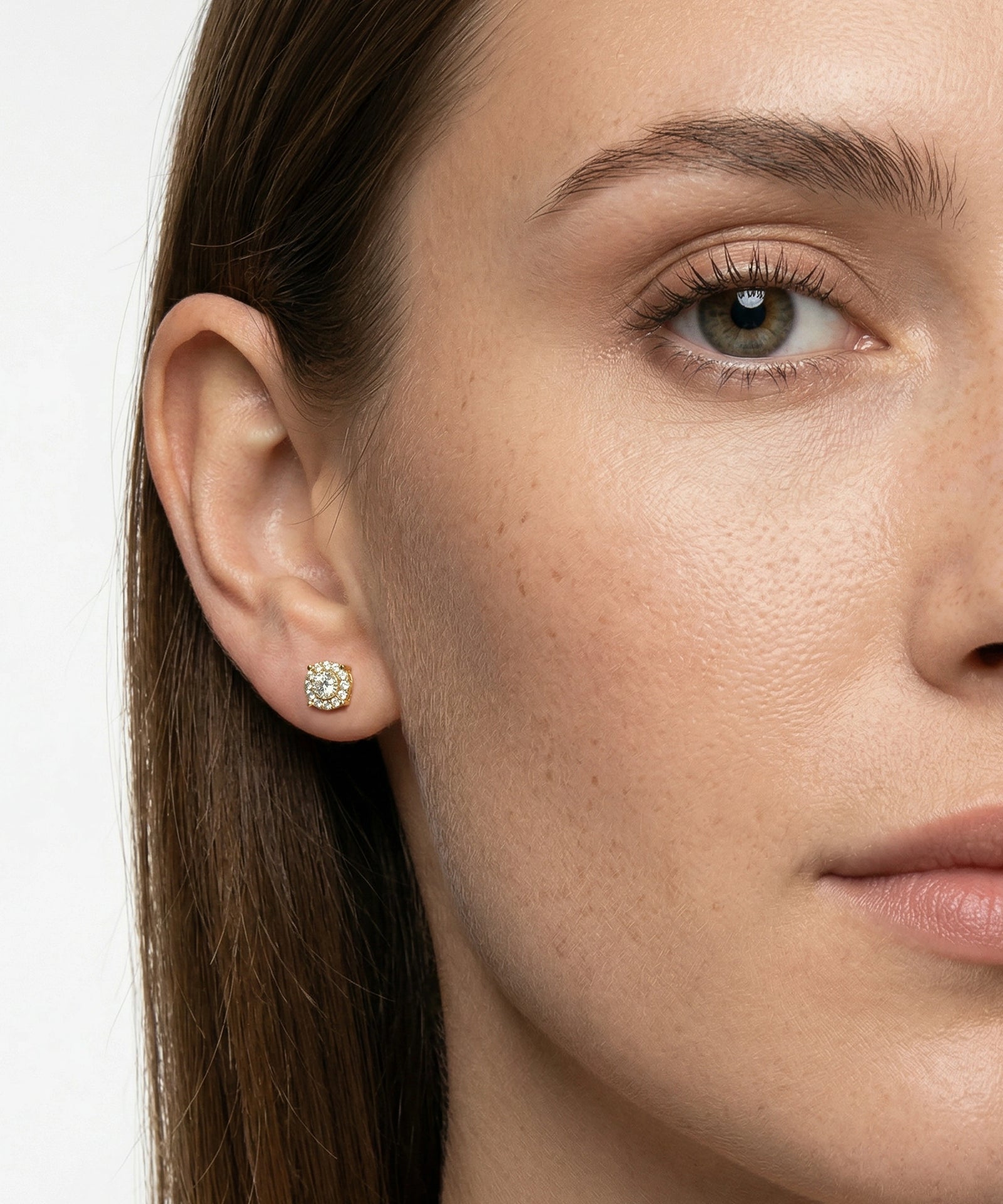 Close-up of a woman's face wearing a diamond earring on a plain background