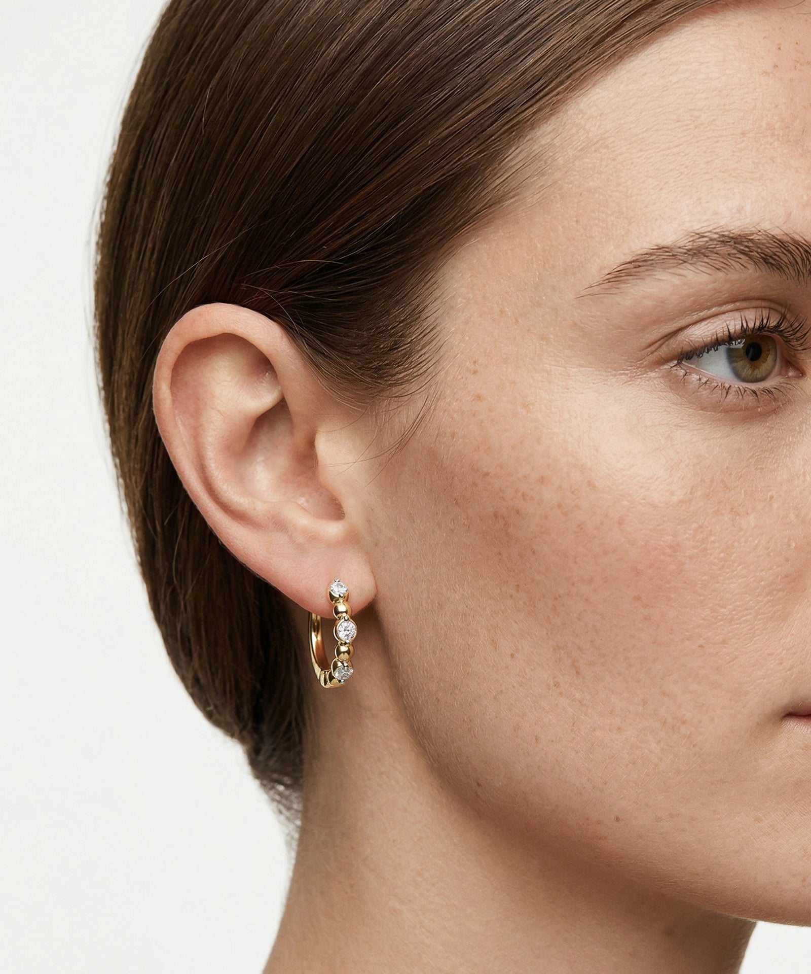 Close-up of a woman wearing gold hoop earrings with small diamonds on a white background