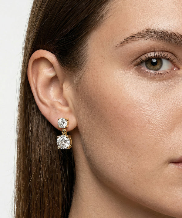 Close-up of a woman wearing gold earrings with a white gemstone.