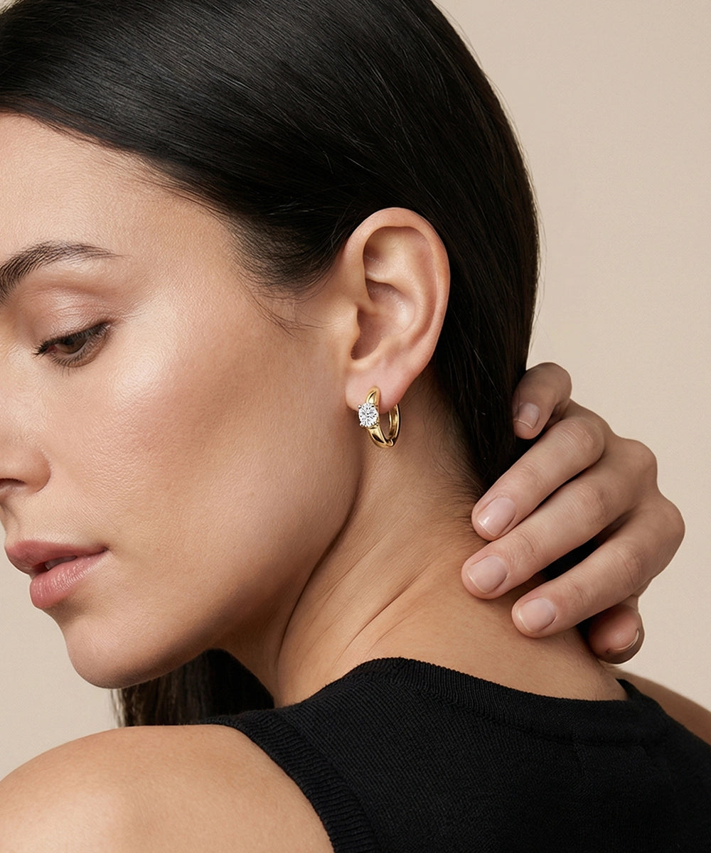 Close-up of a woman wearing gold hoop earrings with a neutral background