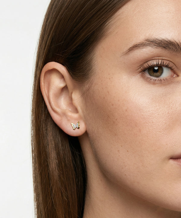 Close-up of a woman wearing butterfly earrings with a plain background
