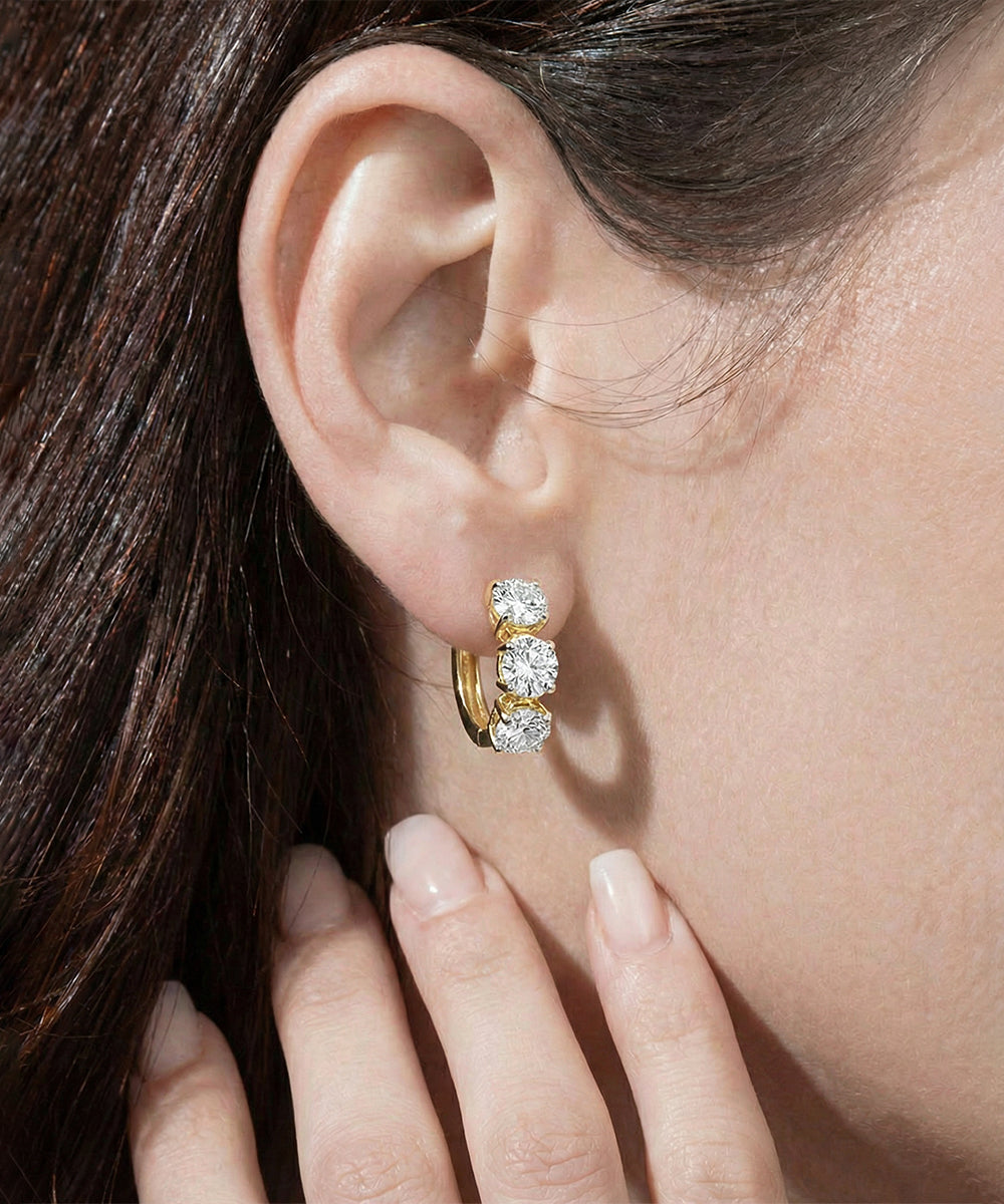 Close-up of a woman wearing diamond hoop earrings with a hand touching her ear.