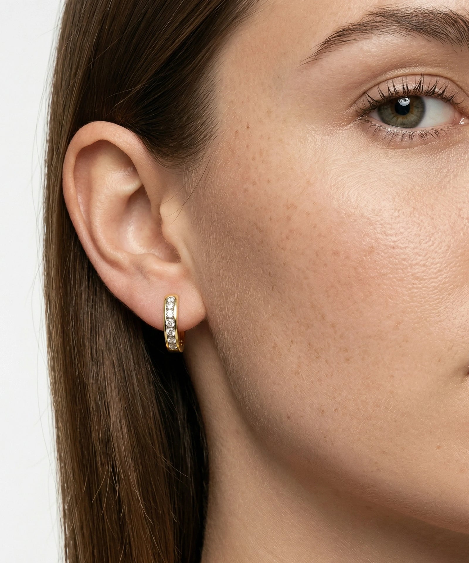 Close-up of a woman wearing gold hoop earrings with a plain background