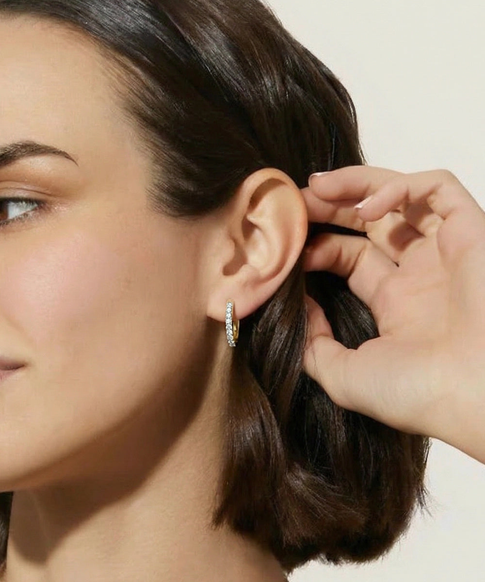Close-up of a woman wearing a diamond hoop earring with a neutral background