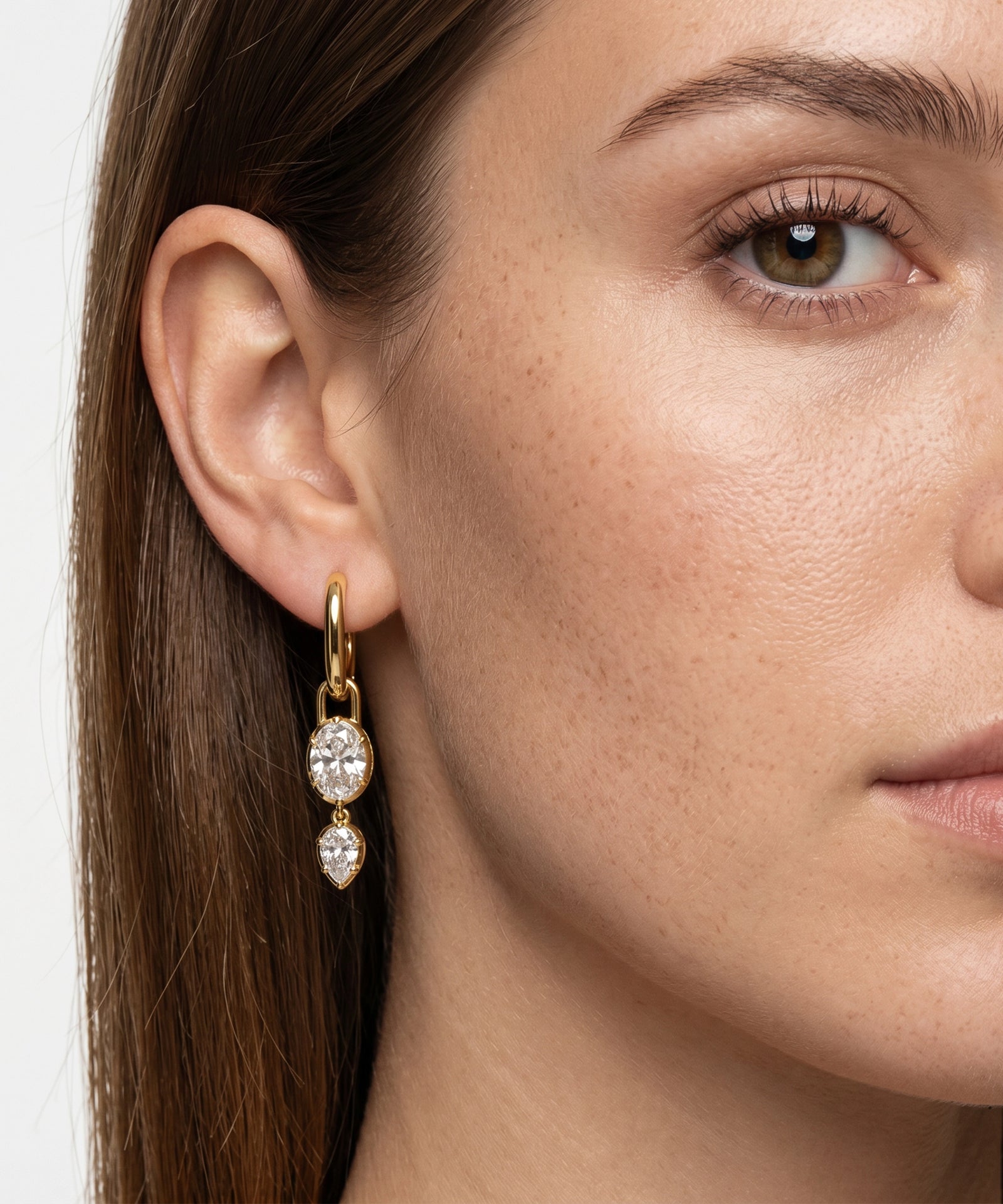 Close-up of a woman wearing gold earrings with clear gemstones.