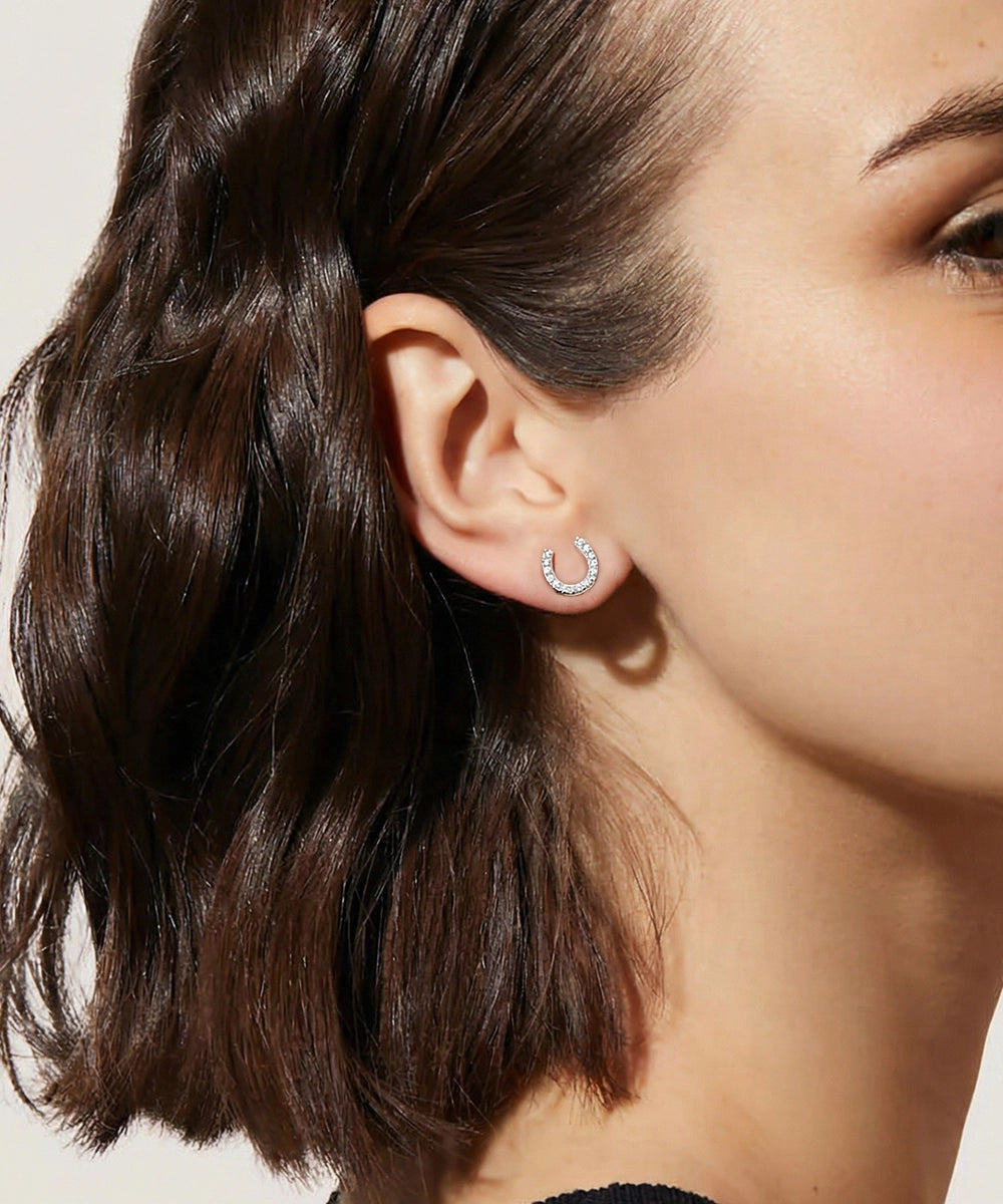 Close-up of a person wearing a silver earring with a clear gemstone.