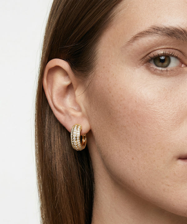 Close-up of a woman wearing gold hoop earrings with a plain background