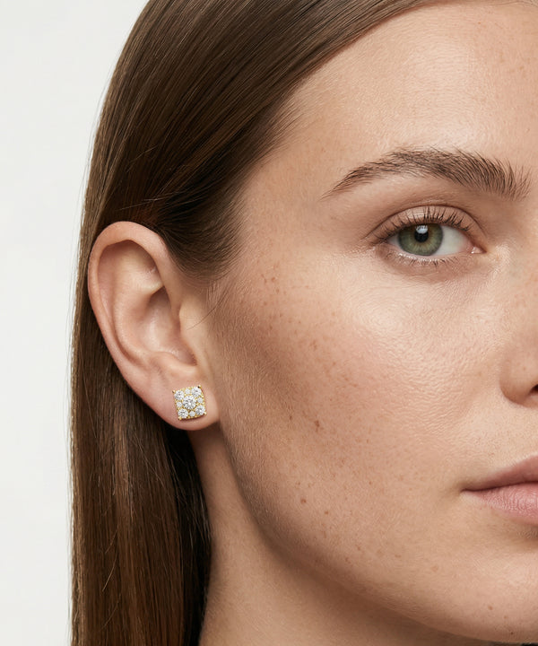 Close-up of a woman's face wearing a diamond earring on a plain background