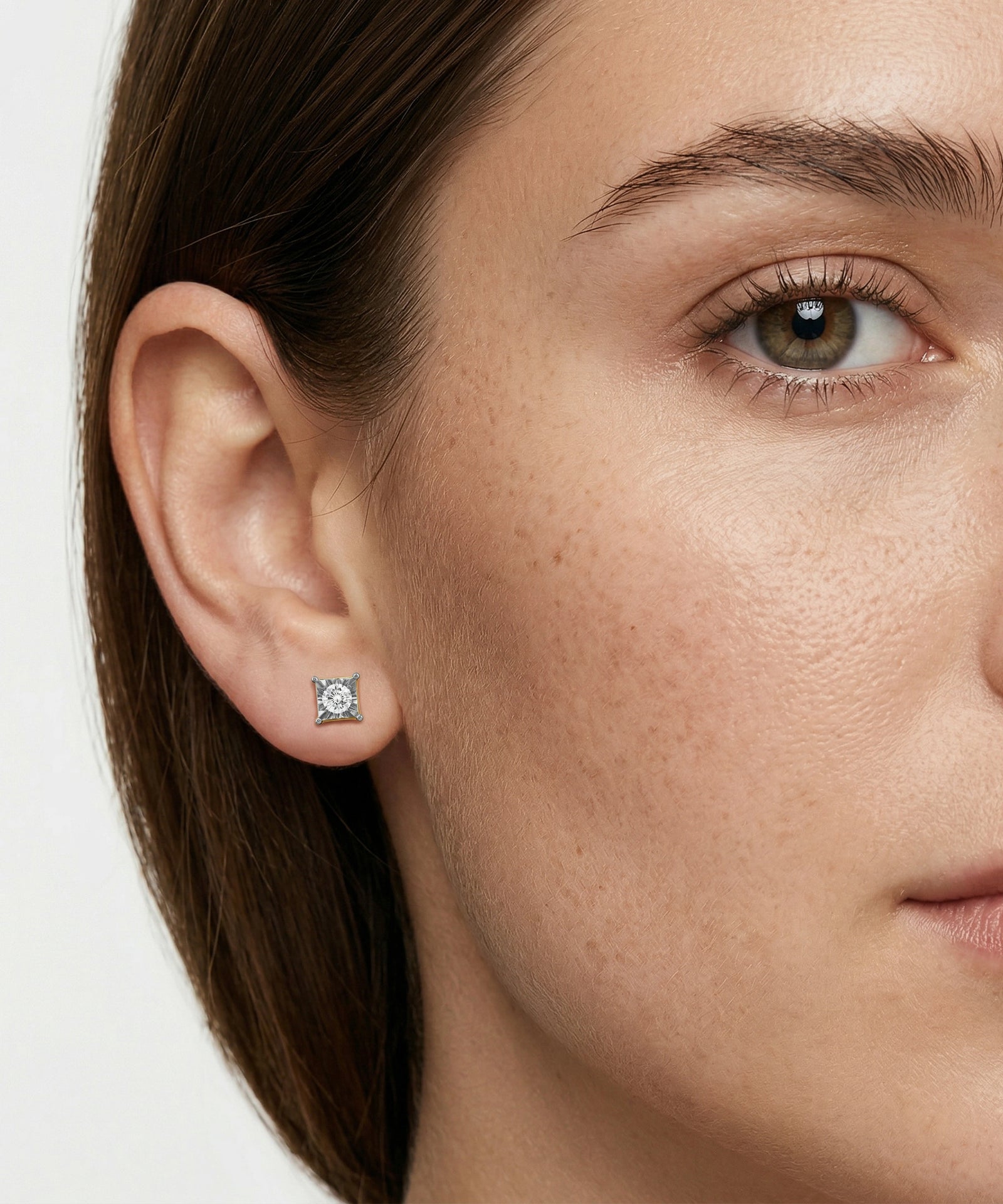 Close-up of a woman wearing a diamond stud earring on a plain background