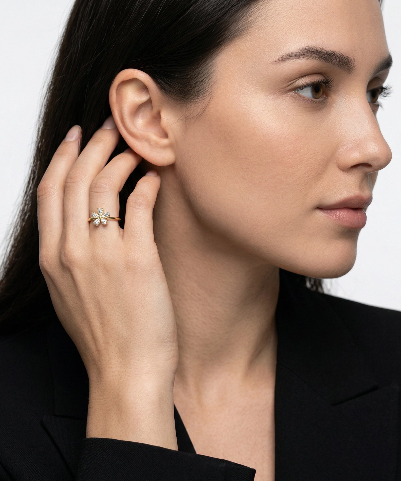Woman wearing a gold ring with a green gemstone on a plain background