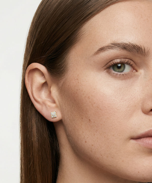 Close-up of a woman's face wearing a diamond earring on a plain background